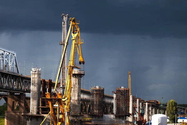 Construction of an automobile bridge over a river against the background of a rainy sky