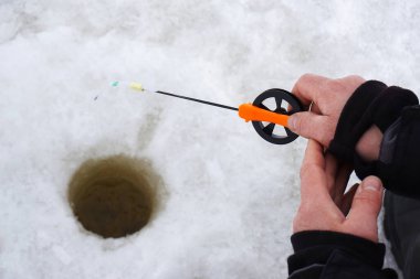 Kışın balık. Balıkçının elleri, delinmiş bir deliğin arka planına bir olta tutuyor. Yakın plan.