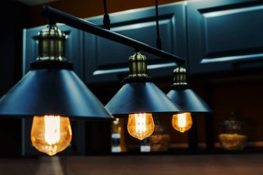 Mutfak setinin arka planında eski tarz metal avizeler var. Parlak lambaları olan karanlık oda.