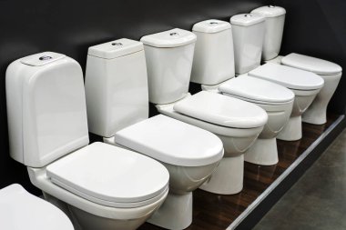 Tesisat dükkanında çeşitli seramik tuvaletler. Alışveriş merkezinin vitrininde bir banyo için geniş bir ürün seçimi. Yakın plan.