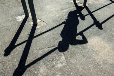 Güç egzersizi sırasında asfaltta bir atletin gölgesi. Yazın caddelerdeki eşit olmayan barlarda spor. Tanınmayacak halde. Seçici odak