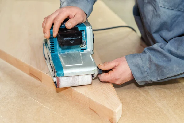 Belt sander setup process. processing of a fragment of a wooden product in the furniture industry. A carpenter makes furniture at a workbench. Close-up. Beyond recognition