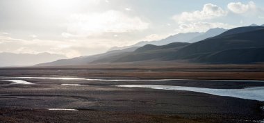Geniş bir dağ vadisi ve arka planda bir nehri olan manzara. Sonbahar güneşinin ışınlarıyla aydınlatılan Asya dağlarındaki nehrin taşkın ovası. 