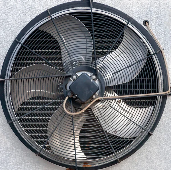 Fan blades, grille, and the outer part of the industrial air conditioner housing. Background with round protective grille and air conditioner engine cooling fan.