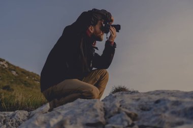 Profilde genç yürüyüşçünün, güneşin doğuşunda fotoğraf çekerken, yumuşak tonlar ve soğuk ışıklarla çekilmiş görüntüleri.