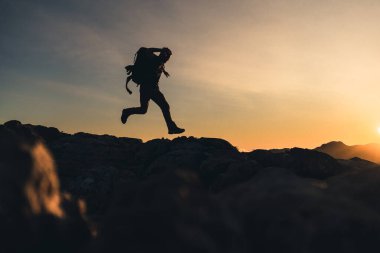 Bir dağın tepesinde yürüyen yürüyüşçü dağın eteğinde koşuyor güzel altın saat günbatımında yoğun bir renk ve mavi gökyüzü sarıyla kaynaşmış büyük bir sırt çantası taşıyor.