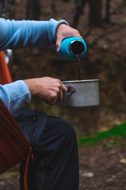 Ormandaki hamakta oturan termostan kahve servisi yapan ellerin yakın çekimi..