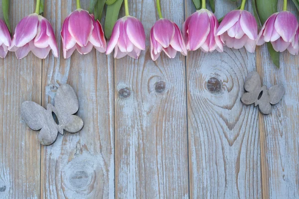 Old grey blue wooden background with pink white tulips border in a row  and empty copy space with wooden spring summer butterflies decoration — Stock Photo, Image