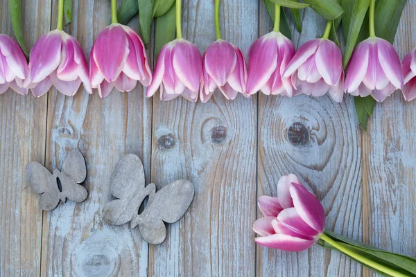 Old grey blue wooden background with pink white tulips border in a row  and empty copy space with wooden spring summer butterflies decoration — Stock Photo, Image