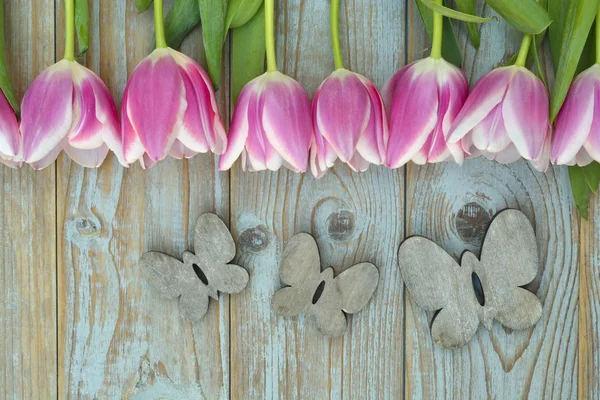 Fundo de madeira azul cinzento velho com borda branca rosa das tulipas em uma fileira e espaço vazio da cópia com decoração de borboletas de madeira do verão da mola — Fotografia de Stock