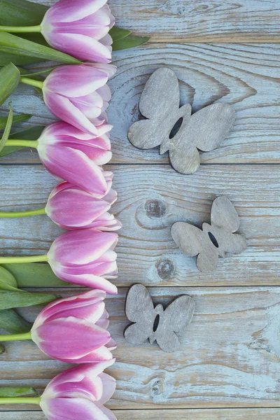 Old grey blue wooden background with pink white tulips border in a row  and empty copy space with wooden spring summer butterflies decoration — Stock Photo, Image