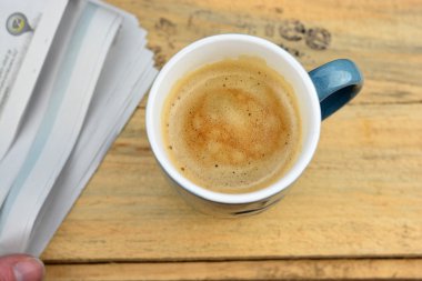 Blue coffee mug with coffee and cream  and news paper on a old used wooden breakfast table with stamps letters