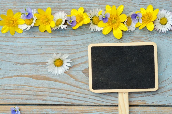 Empty black chalk board on a old used knotted blue , grey wood with daisies and buttercups spring and summer for a serene cheerfull atmosphere flowers — Stock Photo, Image
