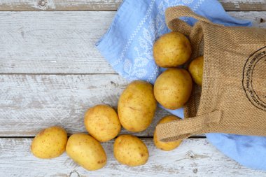 Vintage mavi mutfak çay havlu boş kopya alanı ile bir eski yıpranmış ahşap beyaz raflar zemin üzerine jüt çuval içinde organik taze Çiğ patates