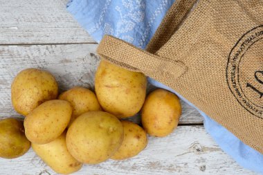 Vintage mavi mutfak çay havlu boş kopya alanı ile bir eski yıpranmış ahşap beyaz raflar zemin üzerine jüt çuval içinde organik taze Çiğ patates