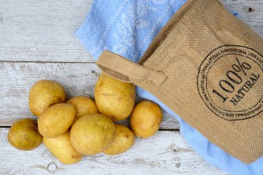 Vintage mavi mutfak çay havlu boş kopya alanı ile bir eski yıpranmış ahşap beyaz raflar zemin üzerine jüt çuval içinde organik taze Çiğ patates