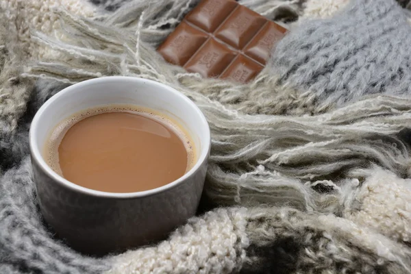 Warme chocolademelk in koffiemok met een grijs, ecru en ivoor gebreide sjaal rond het en chocolade bar — Stockfoto