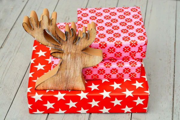 Patrón de flores estrella roja y rosa regalos de Navidad con renos de madera sobre un fondo de estantes de madera — Foto de Stock