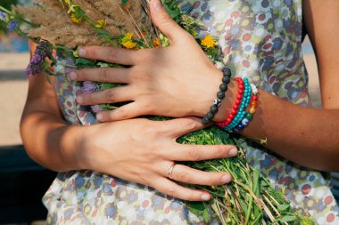 Güneşli bir günde, çok renkli bilezikleri olan kadınların elleri elbiseye bir buket yabani çiçek bastırır.