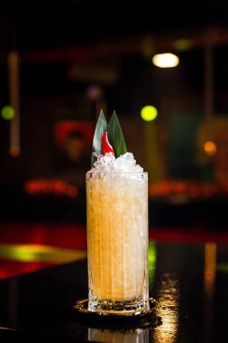 Muz yaprakları ve kırmızı biberle süslenmiş, Collins marka buzlu viski bardağında portakal kokteyli.