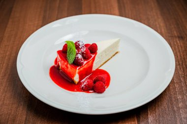 Klasik bir parça cheesecake New York, ahududu şurubu sosu, taze böğürtlen ve nane ile süslenmiş, beyaz tabak.