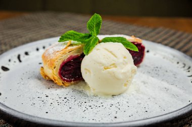 Vanilyalı dondurma ve beyaz tabakta nane filizli vişneli turta.