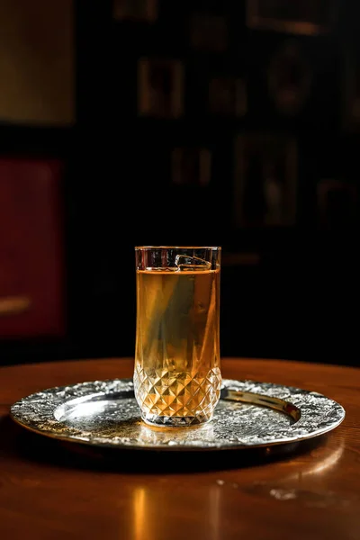 A long drink cocktail with ice in a vintage highball glass on a silver tray