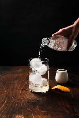 Portakal suyuyla espresso toniği hazırlıyorum. Buz küreleriyle dolu viski bardağına tonik döken bir el.. 