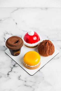 Açık beyaz mermer zemin üzerinde bir krema seti. Sarı mango tartelette, kırmızı beyaz tartelette, iki çikolatalı tatlı.