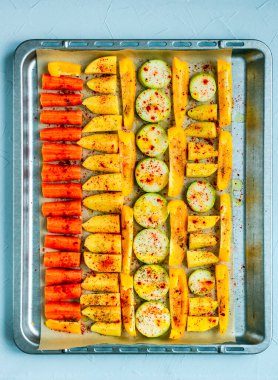 Sebzeler, havuçlar, patatesler, sarı biber ve kabak dilimlenmiş zeytin yağı, tuz, biber, fırınlamadan önce bir tepside. Tepeden çekim.