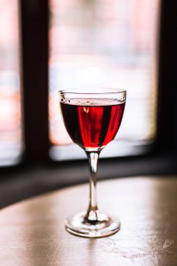 Nick ve Nora bardağında kırmızı alkollü kokteyl, arka ışıkla çekilmiş. Sığ alan derinliğine sahip dikey bir yaşam tarzı fotoğrafı.