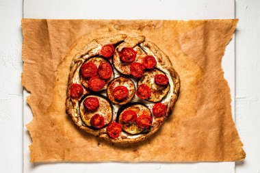 Bir galet ya da turta, ricotta peyniri, patlıcan ve kiraz domatesli fırın kağıdı ve beyaz ahşap tahta, yukarıdan manzara.