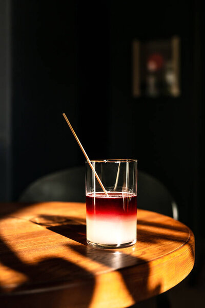 A sweet and sour refreshing blackberry gin bramble cocktail in a highball glass without ice in direct hard sunlight with long shadows, on a wooden table