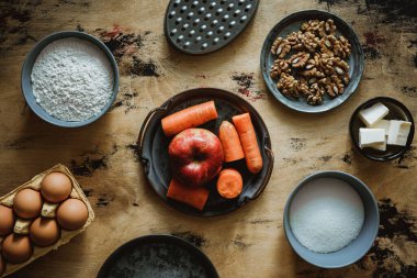 Elmalı havuçlu cevizli kek tarifi. Malzemeler ahşap masada. Un, şeker, tereyağı, yumurta. Öğütücü. 