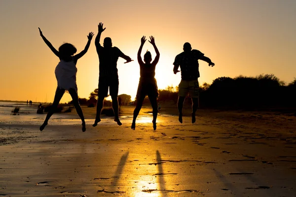 silhouette of a group of young friends who are happy while having fun jumping and running on the beach at sunset during summer vacation