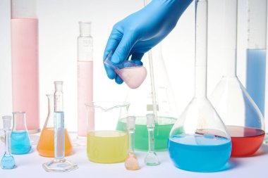 Kimyasal laboratuvar ekipmanları kullanan mavi koruyucu eldivenli bilim adamı eli. Laboratuvar camları, deney tüpleri farklı renklerde reaktörler ve maddelerle dolu..