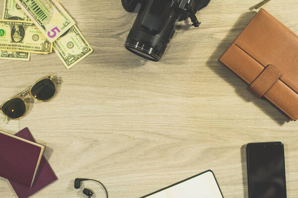 top view of travel accessories. Camera, foreign currency, sunglasses, passports, headphones, notebook, agenda and mobile on wooden table. travel organization and preparation concept. copy space in the center