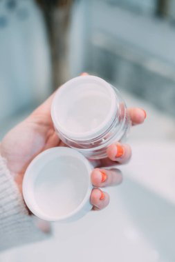 Günlük rutininde açık cam bir yüz kremi kavanozu tutan genç bir kadının eli. bakım ve güzellik konsepti