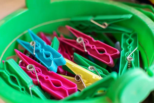 Colorful plastic pegs inside a green plastic basket close up.