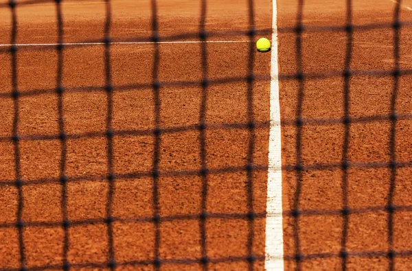 Balle de tennis sur terrain de tennis. Vue à travers le filet — Photo