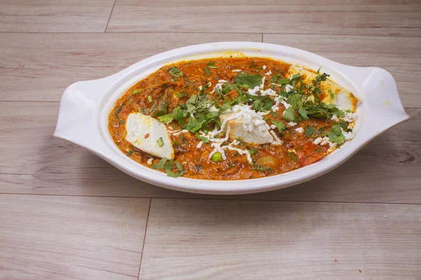 Hint yemeği Paneer Masala ya da Paneer Lachhedar ahşap arka planda kasede servis edilir.