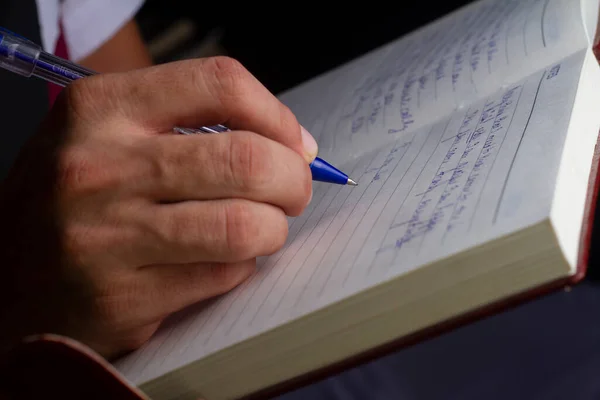 Bir adam not defterine mavi kalemle yazıyor. Seçici bir odaklanma.