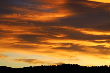 Şafakta dağların üzerinde dramatik bir gökyüzü. Gün doğmadan önce, güneş İskandinavya 'nın ormanı ve ormanlık ufuk çizgisinde batar. Şiddetli altın bulut yanan bir alev gibidir..