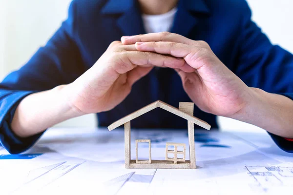 Emlakçı ya da sigortacı ev modelini korumak için jestler yapıyor. Emlak konut sigortası koruma kavramı.