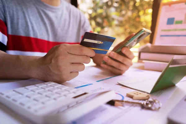 Genç adam kredi kartı tutuyor ve online alışveriş, e-ticaret, internet bankacılığı, harçlık için cep telefonu kullanıyor. İnternet üzerinden alışveriş hizmeti kavramı ve eve servis sunar.