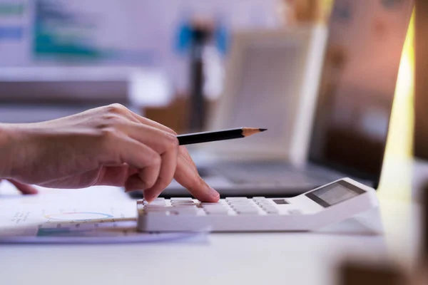 Kapatın, İş adamı ya da Profesyonel Girişimcilik elinde bir kalem tutuyor ve dizüstü bilgisayar, kağıt raporu, gelir grafiği ile hesap makinesine basıyor.