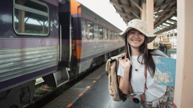 Portre, Asyalı kadın turist gülümseyen ve kameraya bakan sırt çantası, turist haritası, tren istasyonundaki kamera. Seyahat ve ulaşım kavramı.