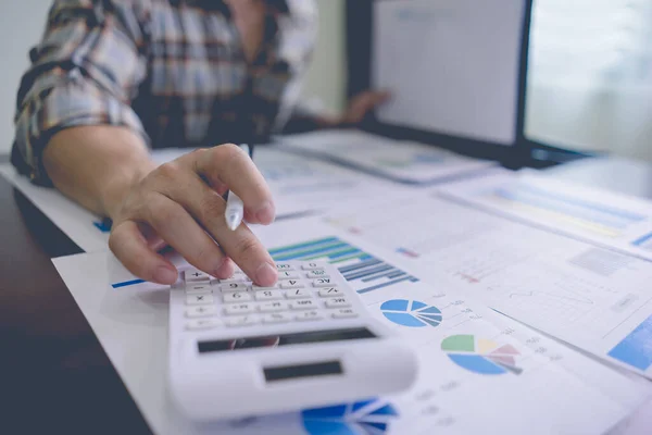 İş adamı ya da Muhasebeci, tablo üzerindeki bir dizinden gelen mali bilgileri grafik istatistikleri, şirket kazancı verileri, gelir ve zarar istatistikleri ile hesaplamak için bir hesap makinesi kullanıyor