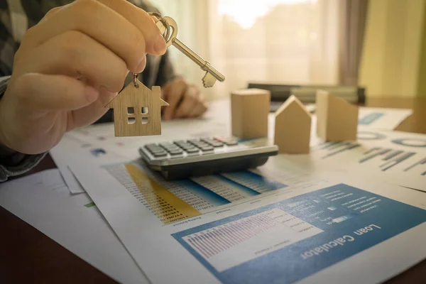 The concept for real estate. Real estate agent holding house key on table with calculator, house designs document, model house.