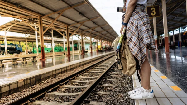 Genç kız gezgin kadın sırt çantası, kamera, seyahat haritası, şapka yürüyüşü ve tren istasyonunda tren bekliyor..